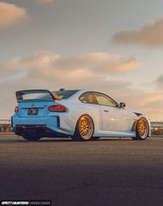 the rear end of a white sports car parked in a parking lot with cloudy skies behind it