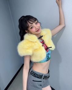 a young woman posing for the camera in a short skirt and cropped top with yellow fur collar