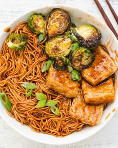 a bowl filled with noodles and vegetables next to chopsticks on a white table