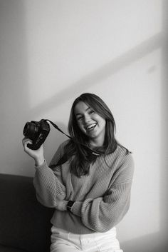 black and white photograph of a woman holding a camera in her right hand, smiling