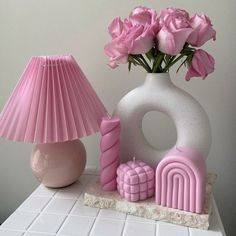 pink roses are in a vase next to a lamp and other items on a table