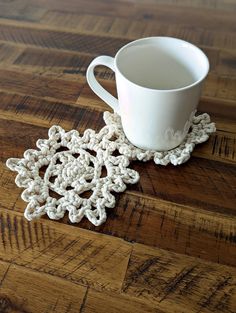 a white coffee cup sitting on top of a wooden table next to a crocheted doily