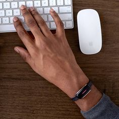 a person's hand on a keyboard next to a computer mouse and apple watch