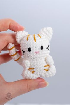 a small white crocheted cat sitting in someone's hand