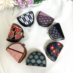 six small purses sitting on top of a white table next to flowers and a vase