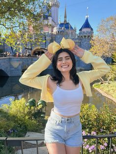 a woman posing in front of a castle with her hands on her head and smiling at the camera