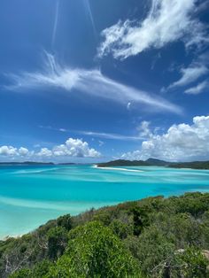 the ocean is blue with white sand and green trees on both sides, under a partly cloudy sky