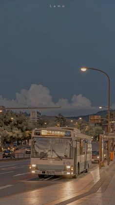 a bus driving down a street next to a traffic light at night with clouds in the sky