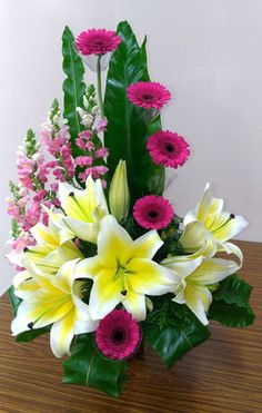 a vase filled with lots of different colored flowers on top of a wooden table next to a green leafy plant