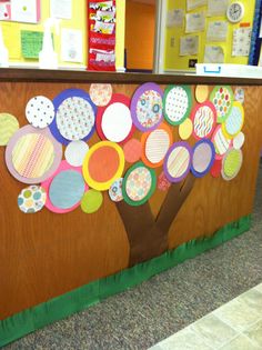 a bulletin board decorated with paper circles and a tree on the front wall in an elementary classroom