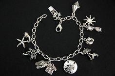 A collection of silver plated beach vacation themed charms have been dispersed around a shimmering silver plated bracelet chain in this handmade charm bracelet. This summer vacation charm bracelet is then completed with a lobster clasp and a 1/2 inch of chain at the end for adjustable sizing. Charms in this bracelet include a tropical drink charm, conch charm, sunglasses charm with sun charm, bare feet charm, beach chair with umbrella charm, sand dollar charm, tropical shirt charm with flipflops Beach Jewelry With Metal Charms, Beach Jewelry With Dangling Metal Charms, Beach Metal Bracelets With Charms, Metal Charm Bracelets For Beach, Silver Beachy Jewelry For Beach Occasions, Beachy Silver Beach Jewelry, Beach Charms Bracelet Jewelry, Bohemian Silver Charm Bracelet For Beach, Silver Bohemian Charm Bracelet For Beach