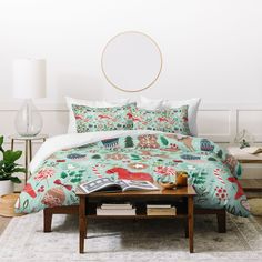 a bed covered in a green floral comforter next to a table with a lamp on it