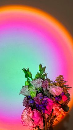 a vase filled with pink and purple flowers on top of a table next to a rainbow colored wall