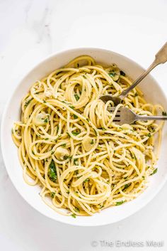 a white bowl filled with pasta and parsley on top of a marble countertop