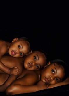 three young children are laying down on a black blanket and posing for the camera with their arms around each other