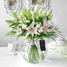 a vase filled with pink and white flowers sitting on top of a table next to framed pictures