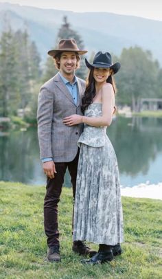 a man and woman standing next to each other in front of a body of water