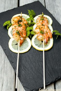 shrimp skewers with lemon slices and parsley on a black slate platter