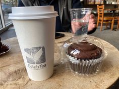 a cup of coffee next to a muffin on a wooden table in a cafe