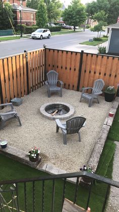 an outdoor fire pit surrounded by lawn chairs and potted plants on the side of a wooden fence