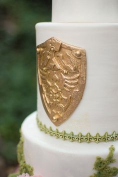 a close up of a white cake with gold decorations on it's sides and flowers around the edges