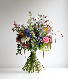 a vase filled with lots of colorful flowers on top of a white table next to a wall