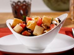 a white bowl filled with pasta and vegetables on top of a red place mat next to a fork