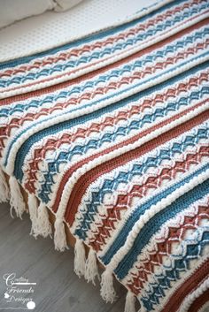 a crocheted blanket is laying on the floor next to a bed with pillows