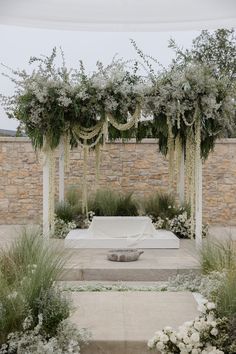 an outdoor ceremony setup with white flowers and greenery on the sides, surrounded by stone walls