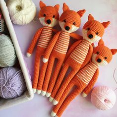 several knitted foxes are laying next to balls of yarn