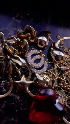 an assortment of jewelry is laying on a table with a red object in the foreground