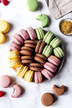 colorful macaroons arranged in a circle on a white marble surface with other macaroons and confections