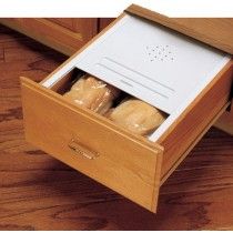 an open drawer with bread in it on the floor next to a wooden counter top