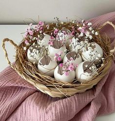 a basket filled with white eggs sitting on top of a pink blanket next to flowers