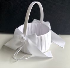 a white basket with a bow on the side and ribbon tied around it, sitting on a table