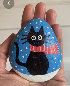 a hand holding a painted rock with a black cat on it