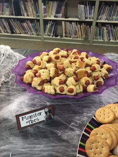 a table topped with lots of food next to a purple plate filled with dogs on top of crackers