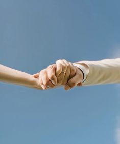 two people holding hands in front of a blue sky and cloud filled sky with only one hand on the other arm