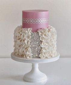 a three tiered cake with white and pink flowers on top, sitting on a pedestal