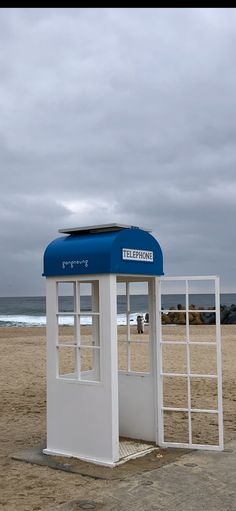 a blue and white phone booth sitting on top of a sandy beach