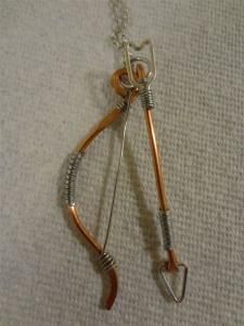 a metal and wood bow and arrow necklace on a white cloth with a silver chain