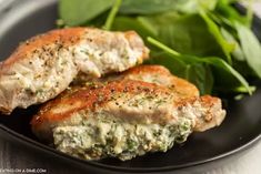 two pieces of meat on a black plate with spinach leaves in the foreground