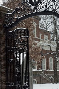 an iron gate with a clock on it in front of a brick building covered in snow