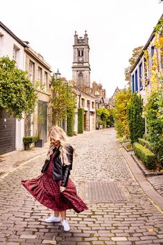 a woman in a red dress and black jacket walking down a cobblestone street