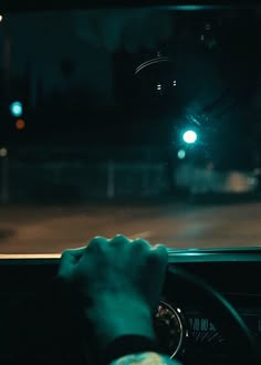 a person driving a car at night in the dark with their hand on the steering wheel