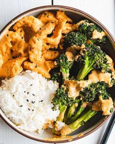 a bowl filled with rice and broccoli covered in sauce next to chopsticks