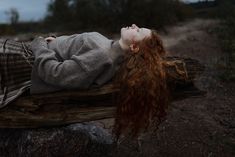 a woman with red hair laying on a log