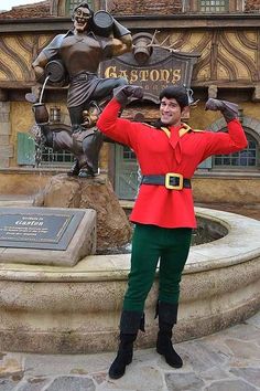 a man dressed in an elf costume standing next to a statue with his hands up