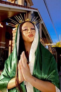 a woman dressed in green and white with her hands folded over her face while standing outside