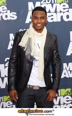 a man in a leather jacket and scarf smiles for the camera on the red carpet